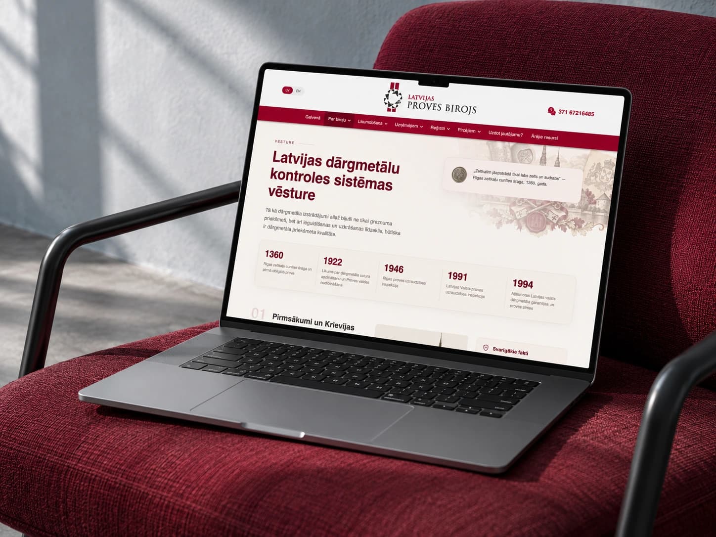 Latvijas proves birojs website on a laptop resting on a burgundy armchair in natural light.